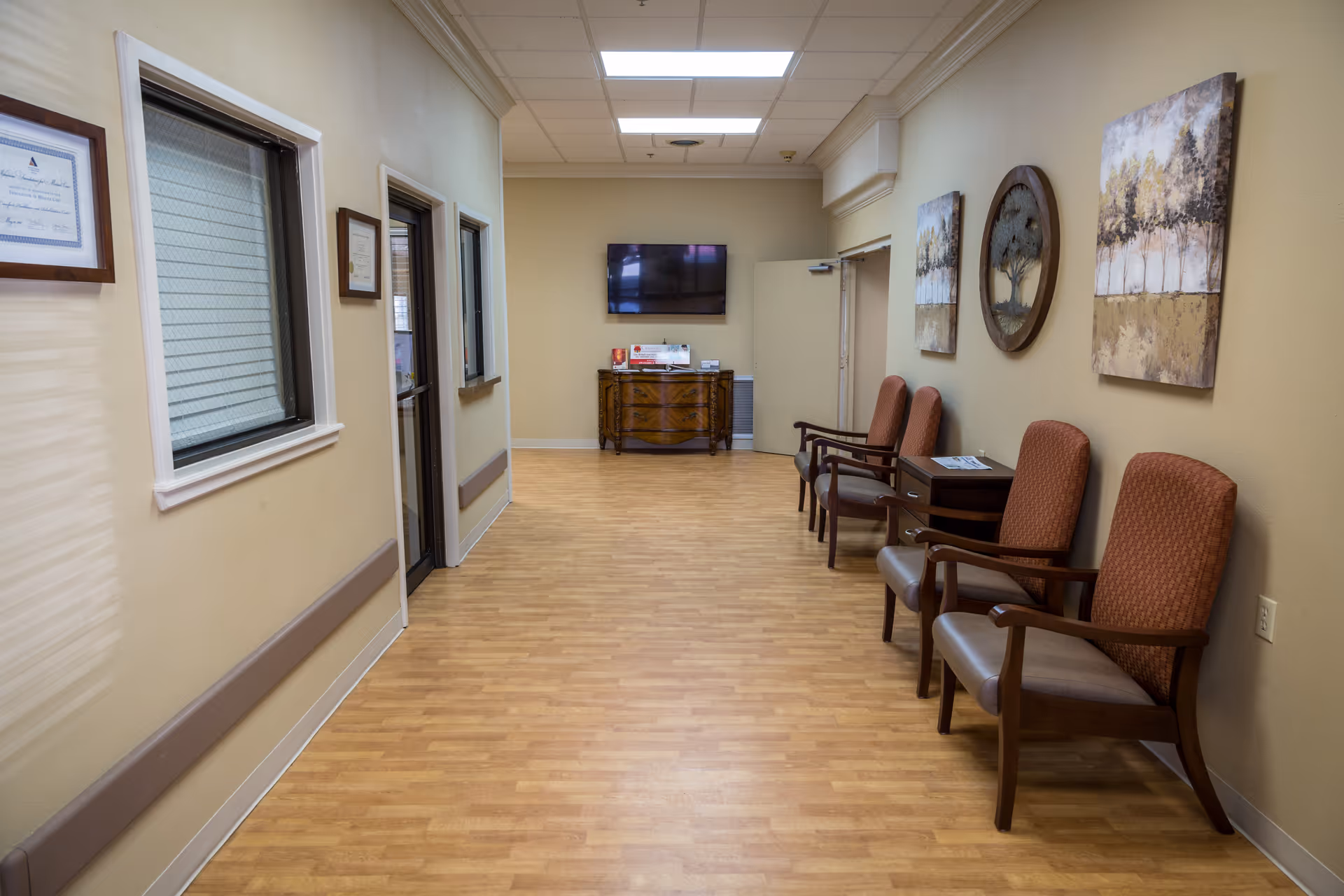 Interior hallway of a senior living facility with chairs and a wall-mounted TV.