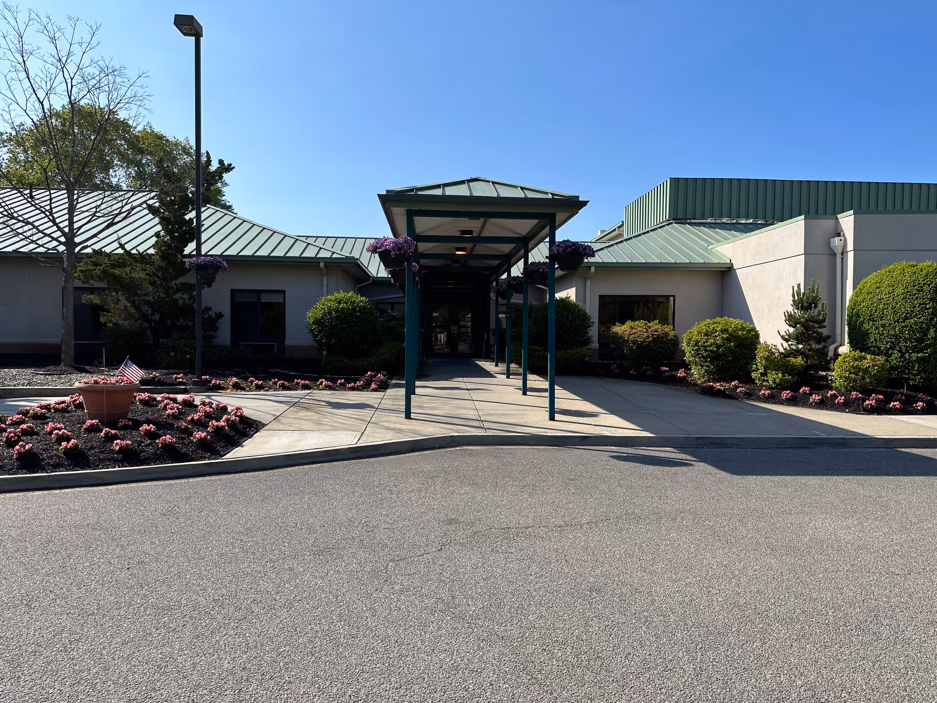 Front entrance of a senior living facility with a covered walkway and landscaped flower beds.