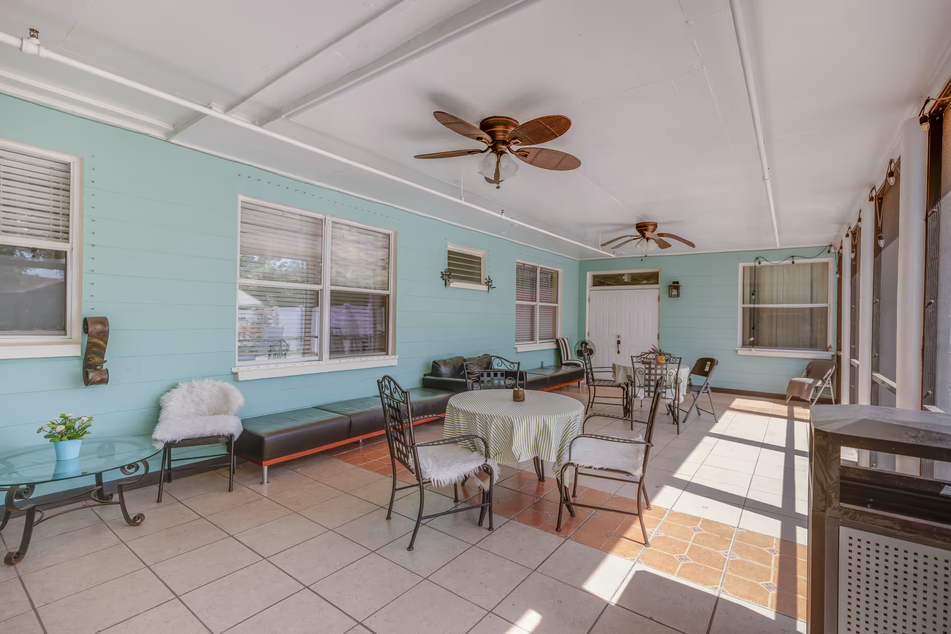 Covered outdoor patio with tables, chairs, ceiling fans, and turquoise walls.