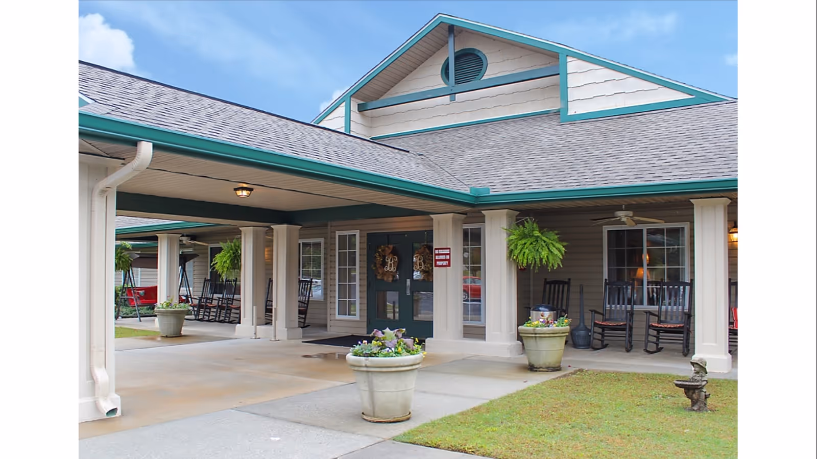 Senior living facility entrance with columns, rocking chairs, and potted plants on a covered porch.