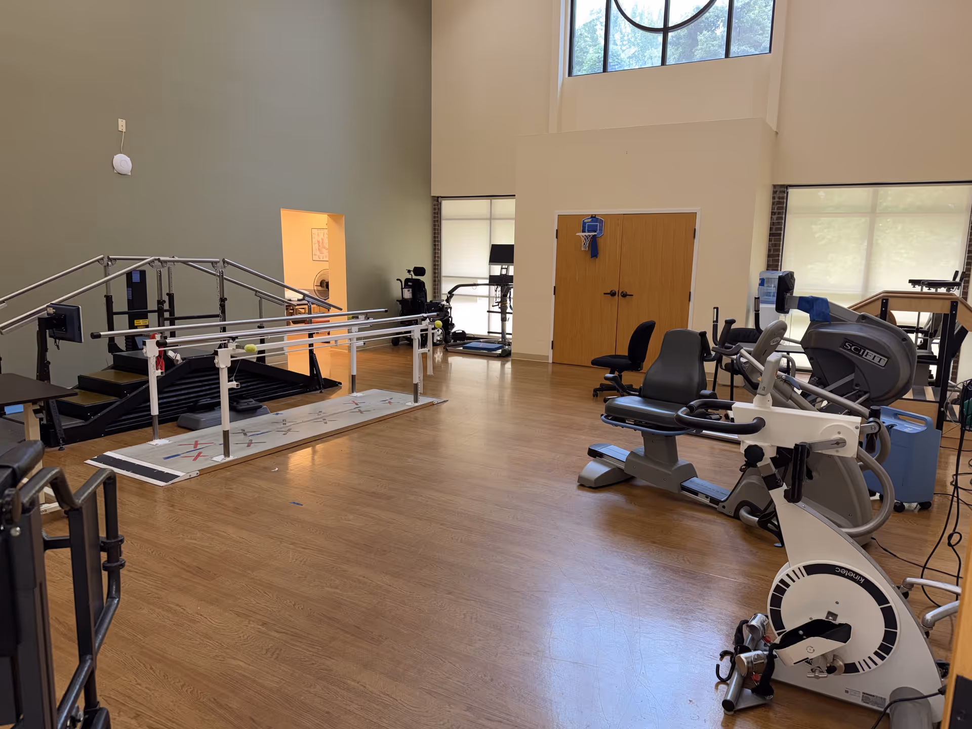 Rehab gym with parallel bars and cardio machines in a bright, spacious room.