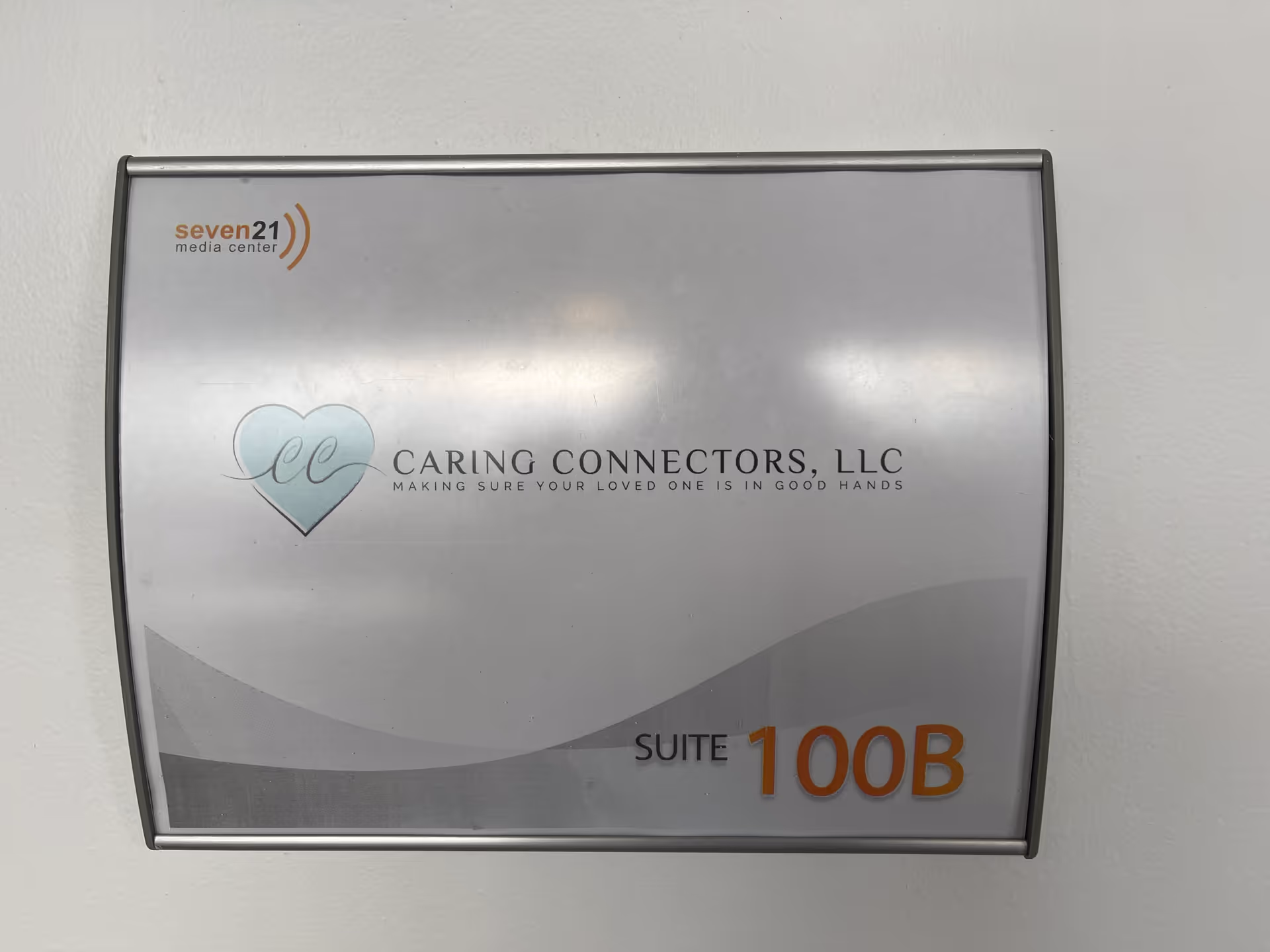 Metal plaque sign displaying Caring Connectors, LLC, Suite 100B, on a light wall.