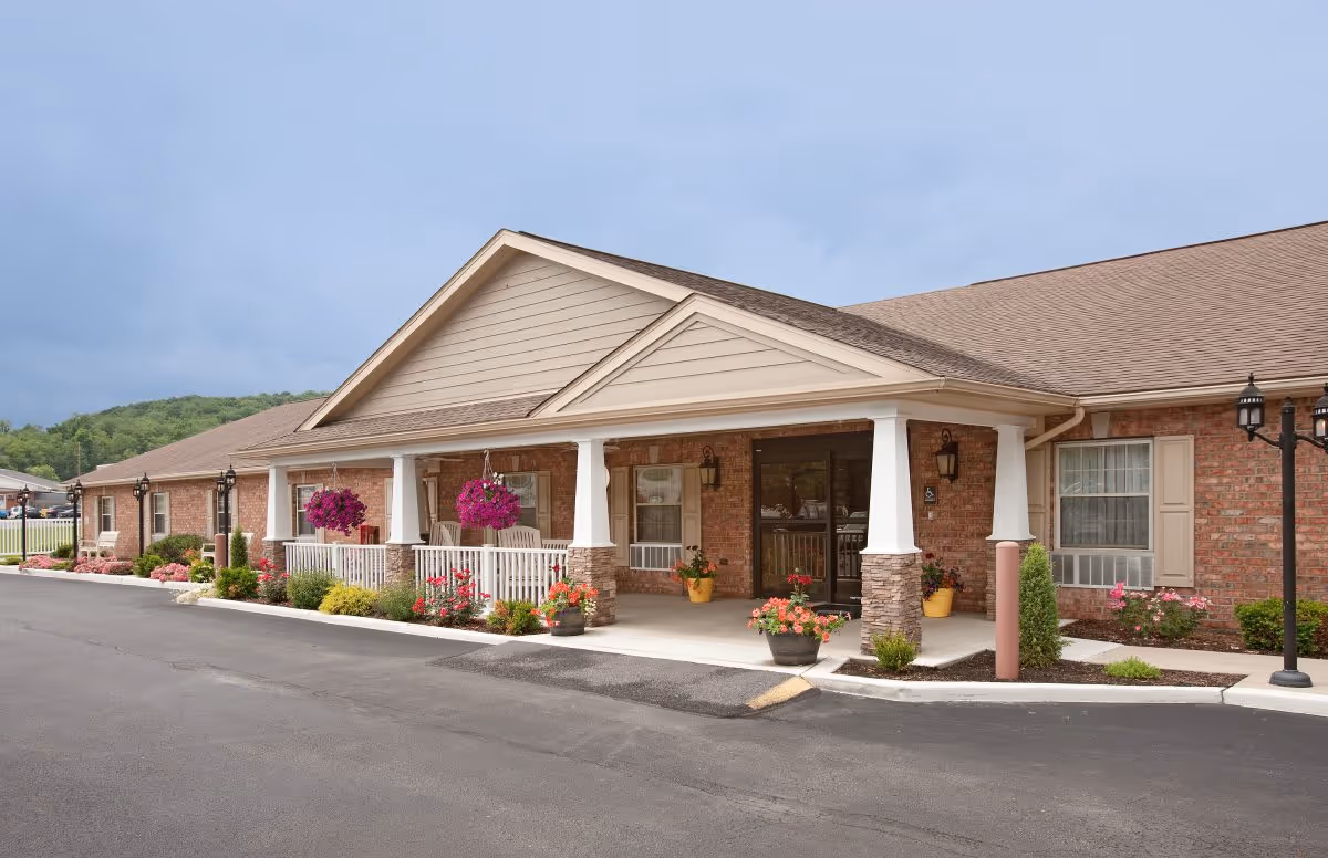 Brick senior living facility exterior with a covered entrance and flower-filled landscaping.