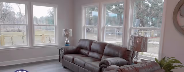 Bright living room with gray leather sofas, large windows, and lamps.