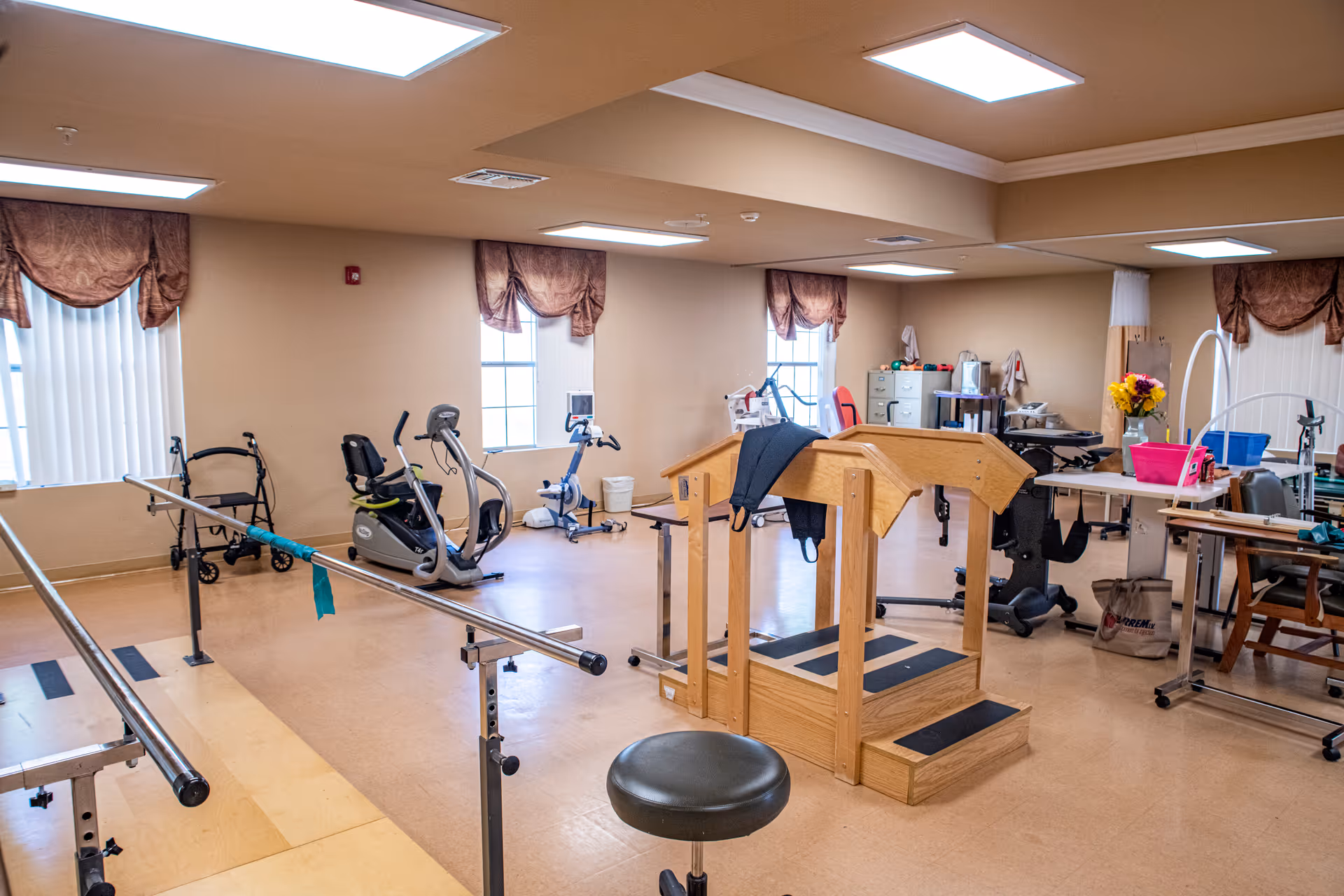 Rehabilitation gym inside a senior living facility with exercise equipment and parallel bars.