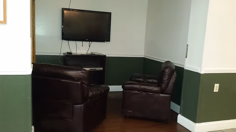 Small living room in a facility with two leather chairs and a wall-mounted TV.