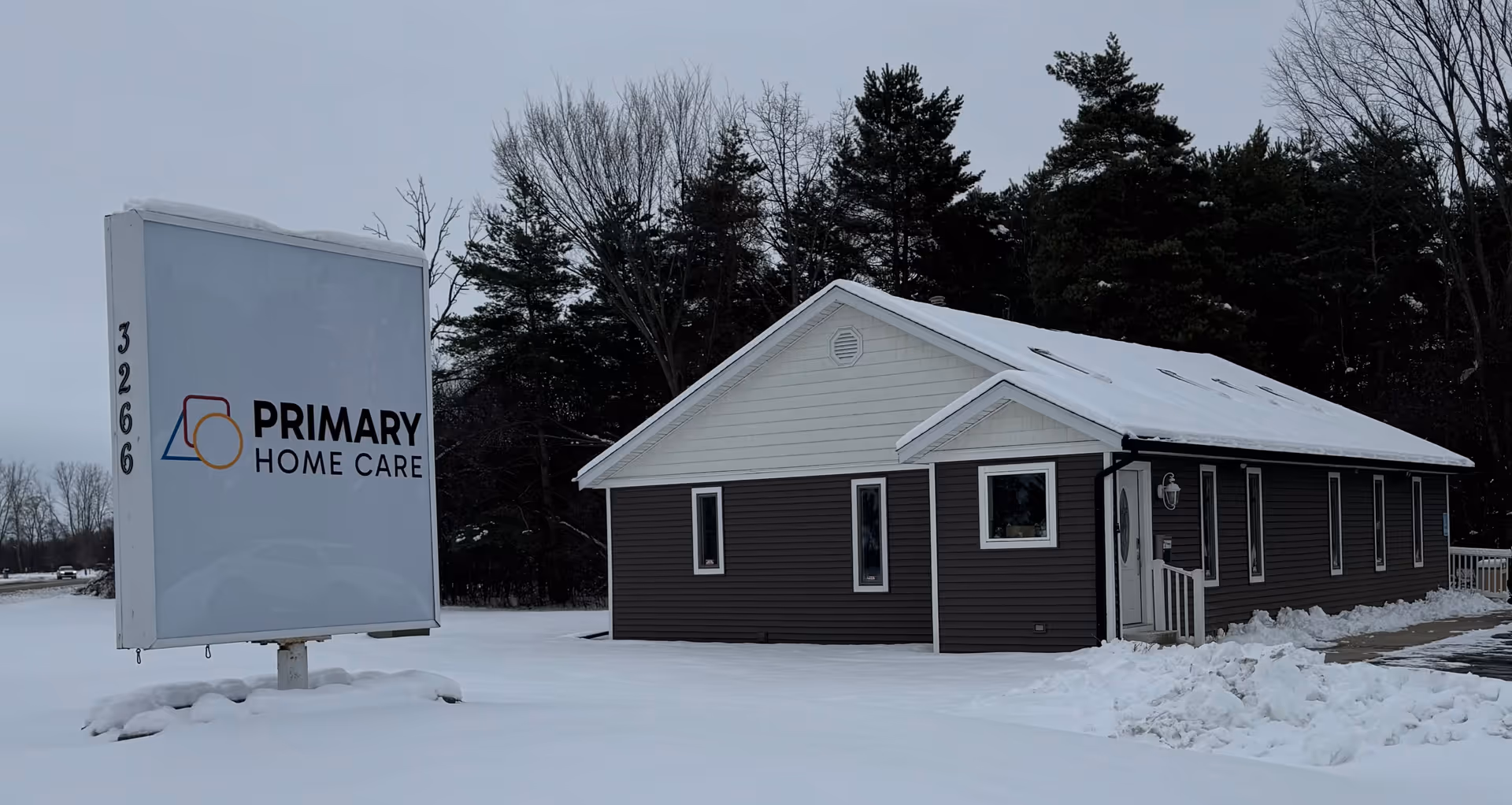 Exterior view of a single-story building with a sign reading Primary Home Care in snow.