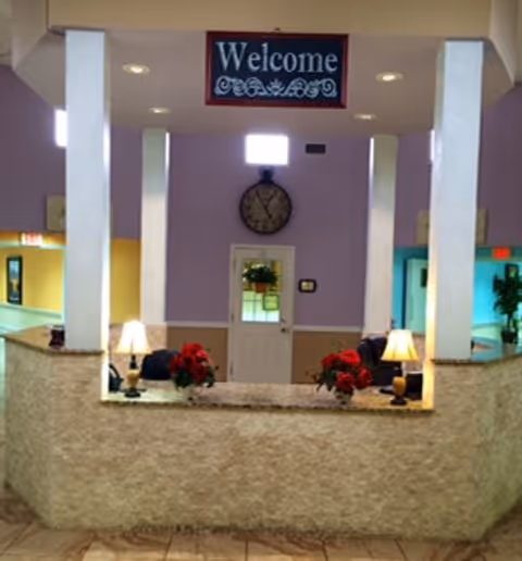 Lobby reception area with columns, a Welcome sign, clock, door, and red poinsettia plants.