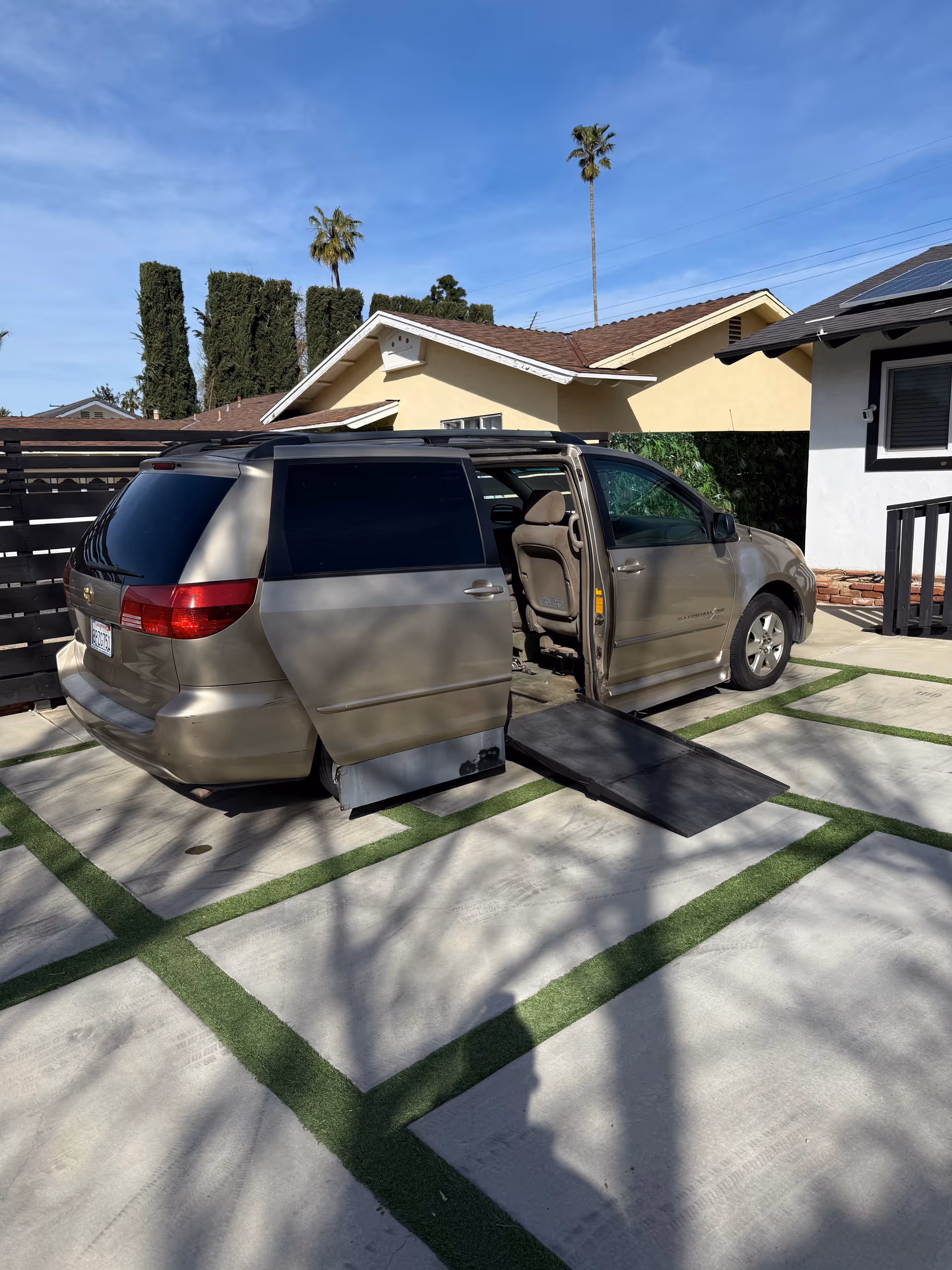 Silver minivan with a side ramp parked in a driveway in front of a house.