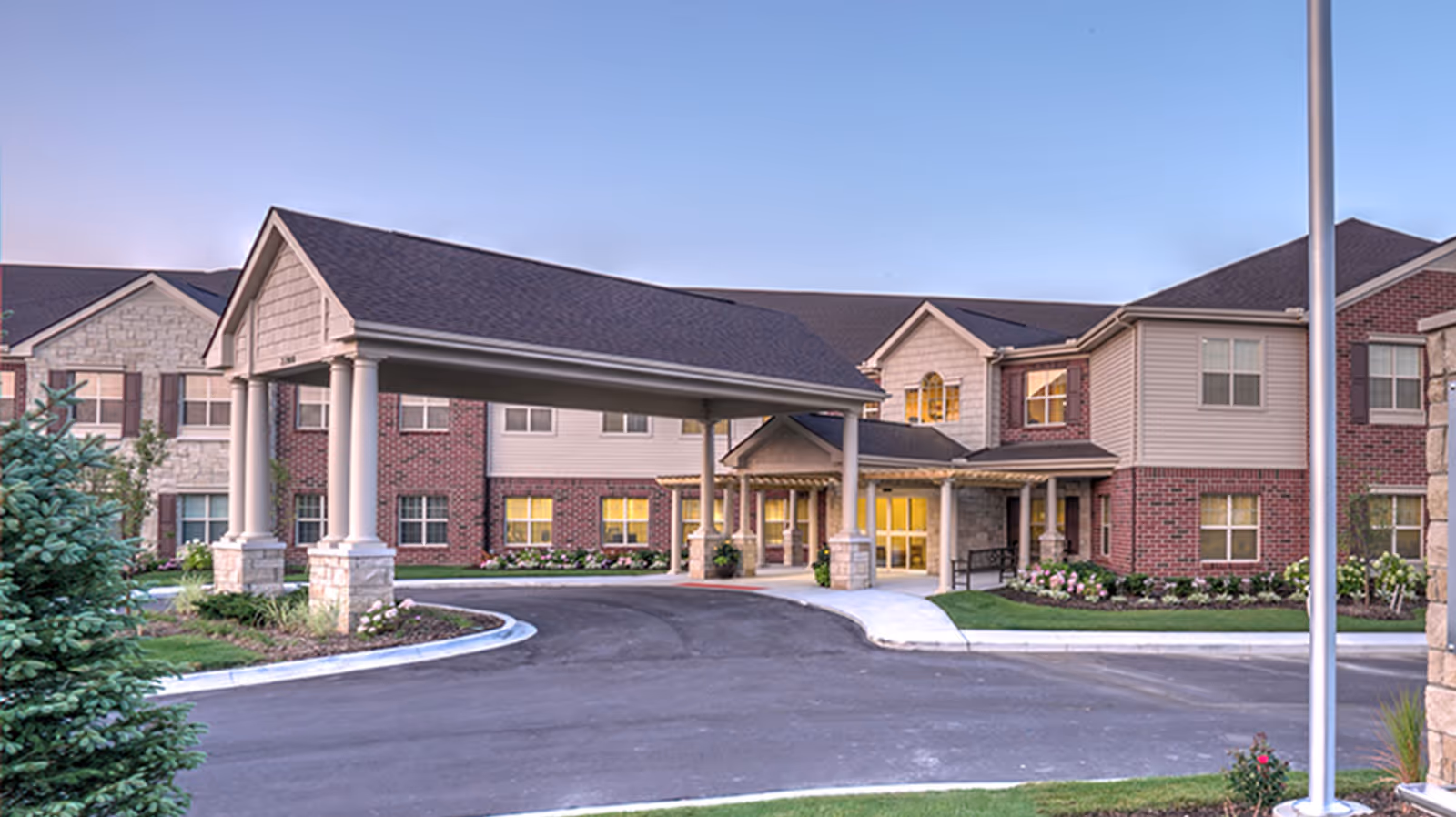 Front entrance of a senior living facility with a covered drive-up portico, circular driveway, and landscaped grounds.