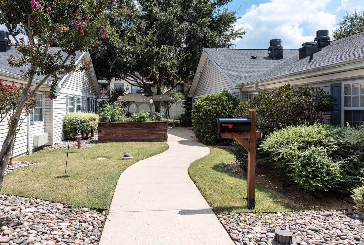 Curved walkway between Arden Courts Richardson buildings, with landscaped shrubs and a raised garden bed.