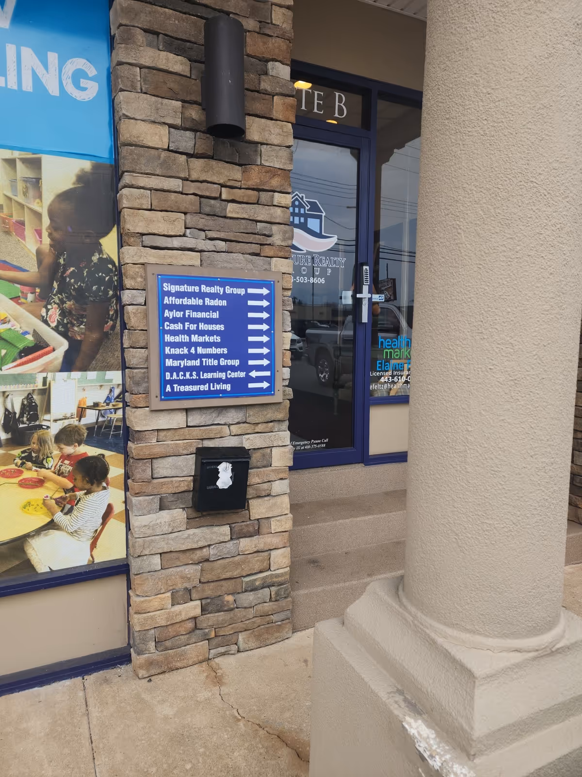 Exterior of A Treasured Living facility with a blue door, stone walls, and directory sign.
