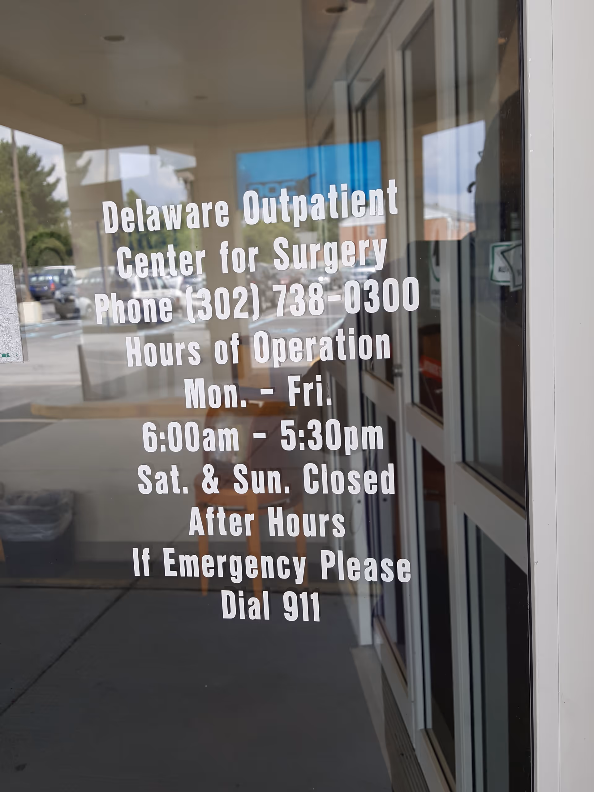 Glass storefront door with large white text displaying Delaware Outpatient Center for Surgery hours.