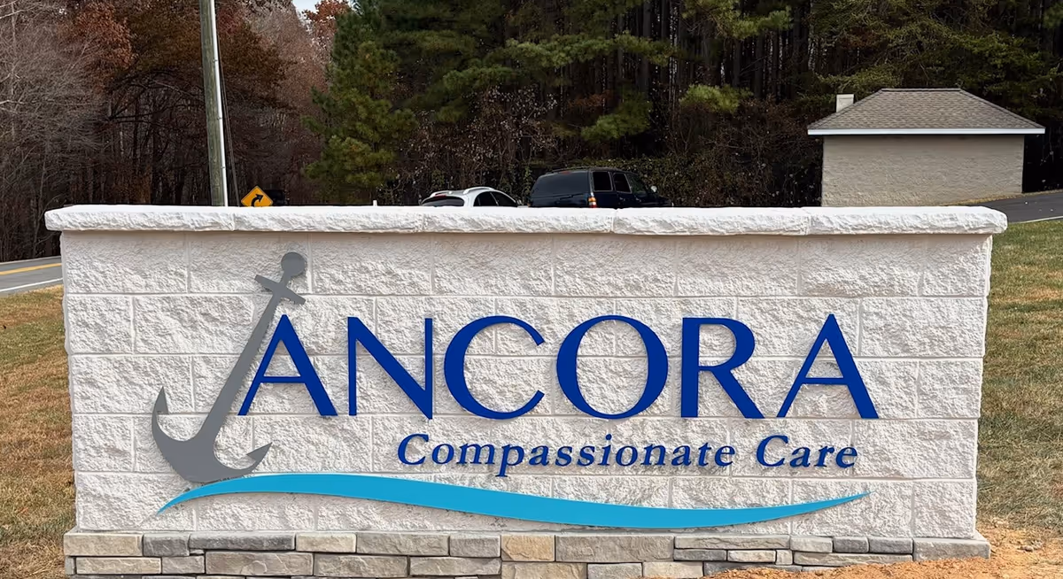 Exterior stone sign displays ANCORA Compassionate Care with an anchor logo.