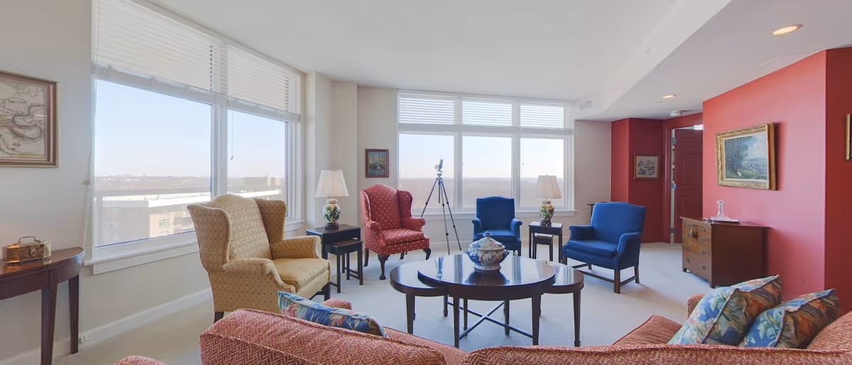 Bright common sitting room with multiple upholstered armchairs, a round coffee table, and large windows.