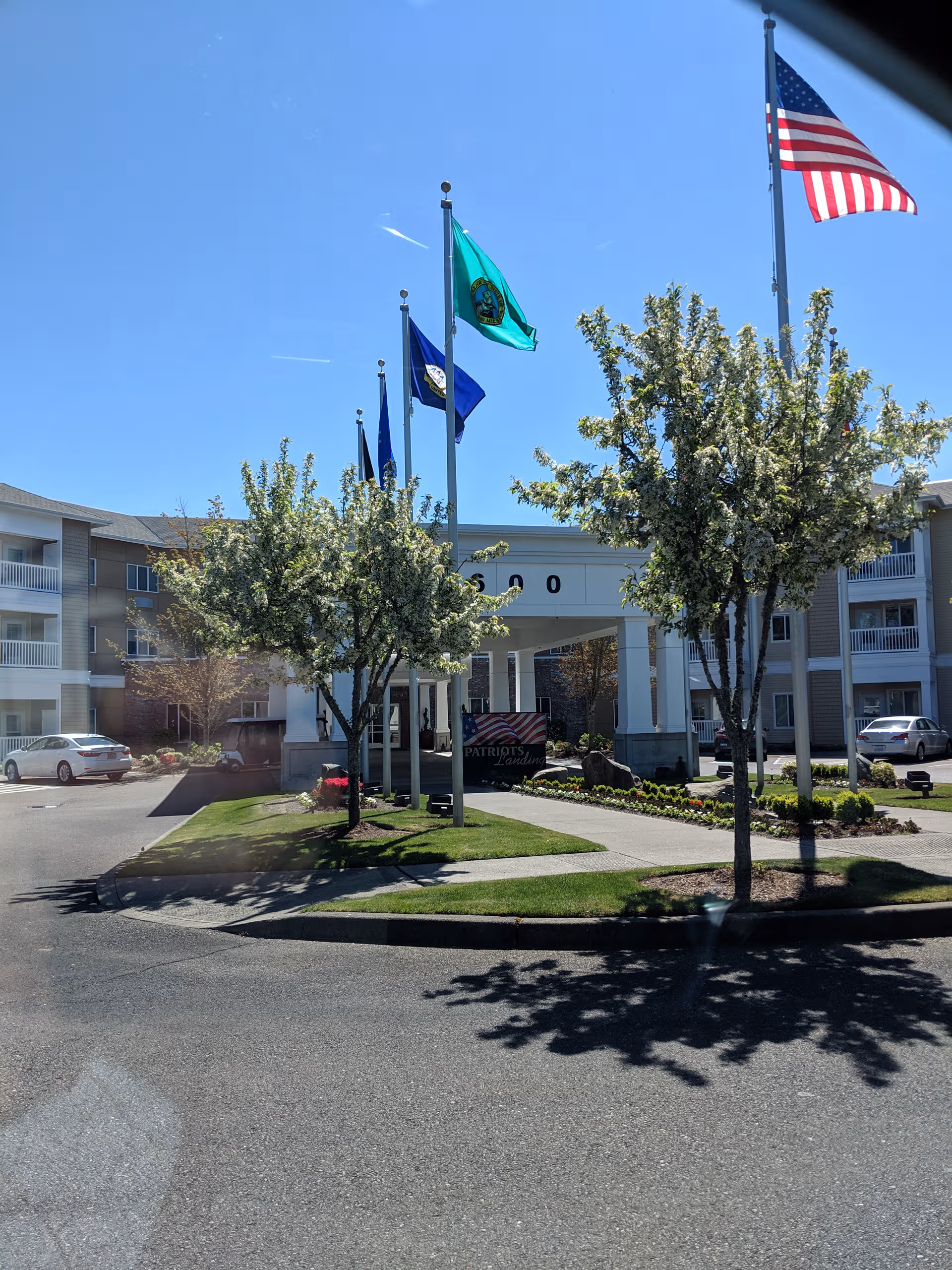 Exterior view of Patriot's Landing senior living facility with flags and landscaped entrance.