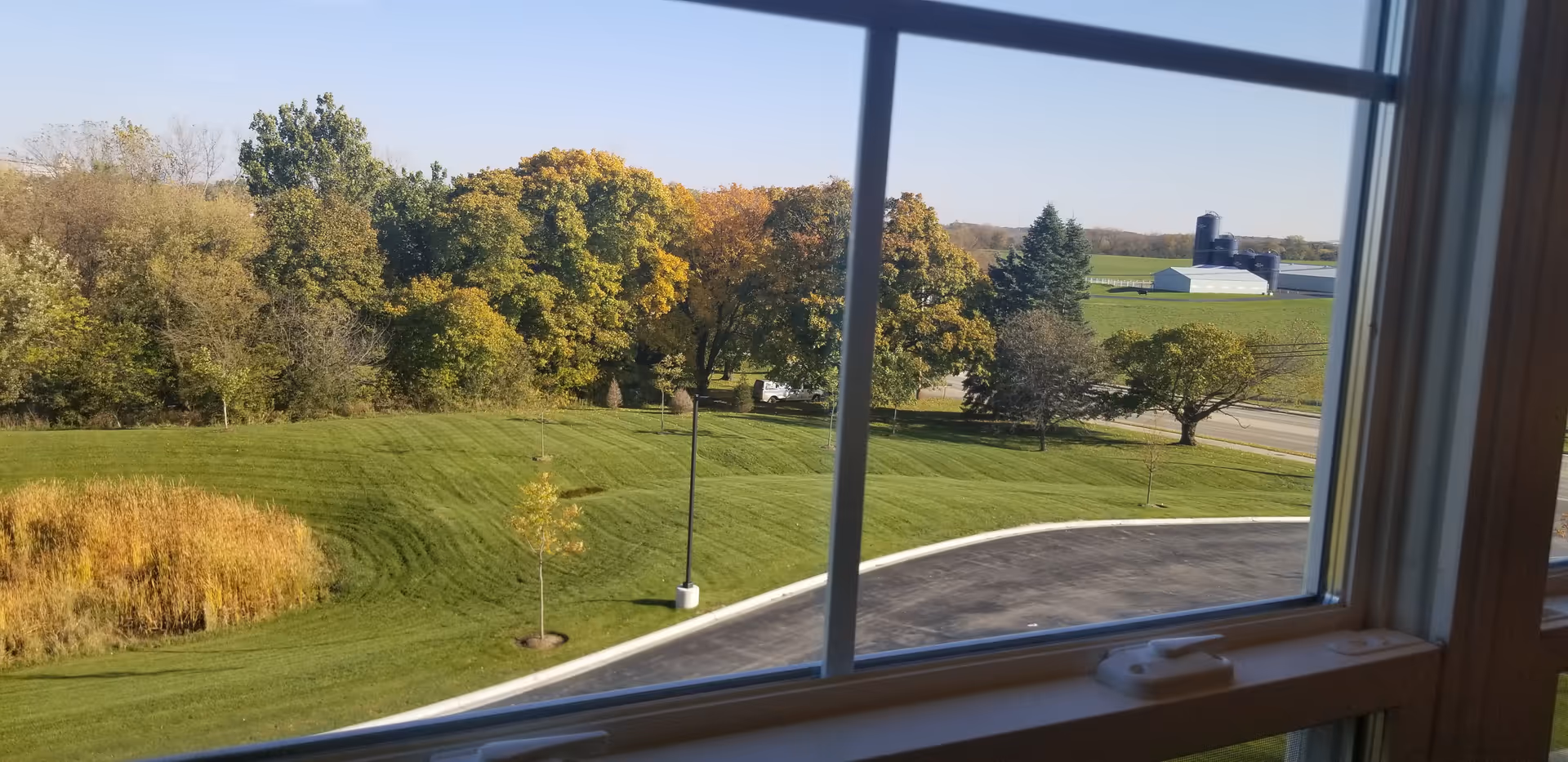 View of a green landscape with trees and a distant farm through a window.