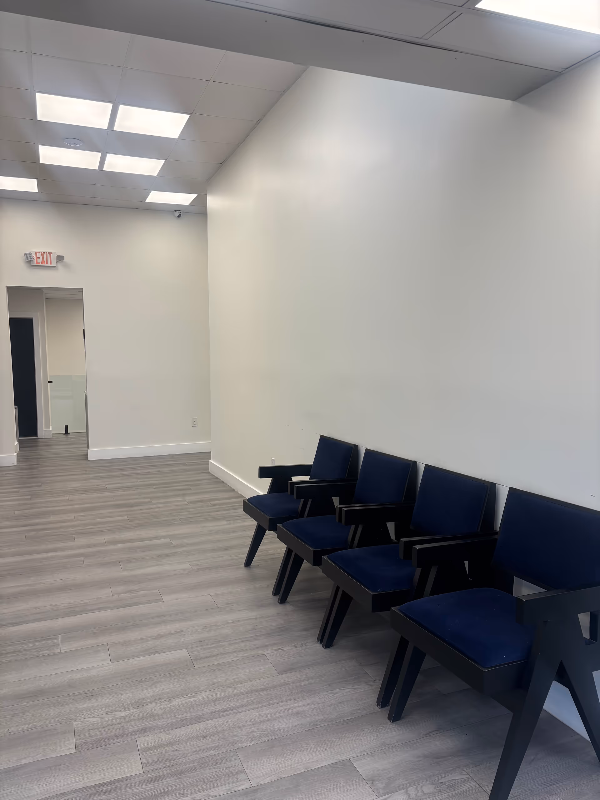 Empty hallway with blue chairs along a white wall in a modern facility.