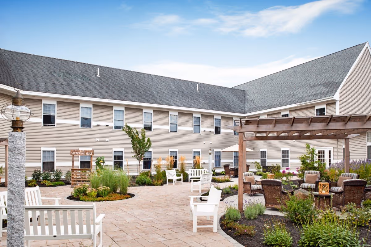 Outdoor courtyard with seating, a pergola, landscaping, and a two-story beige building.