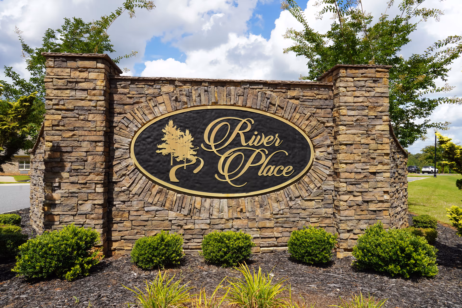 Stone entrance sign reading River Place with landscaped shrubs and trees.