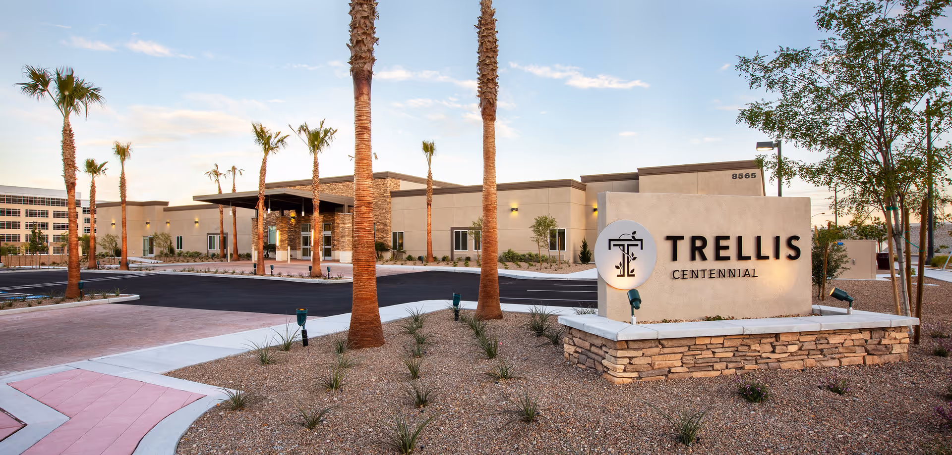 Exterior view of Trellis Centennial senior living facility with sign and palm trees.