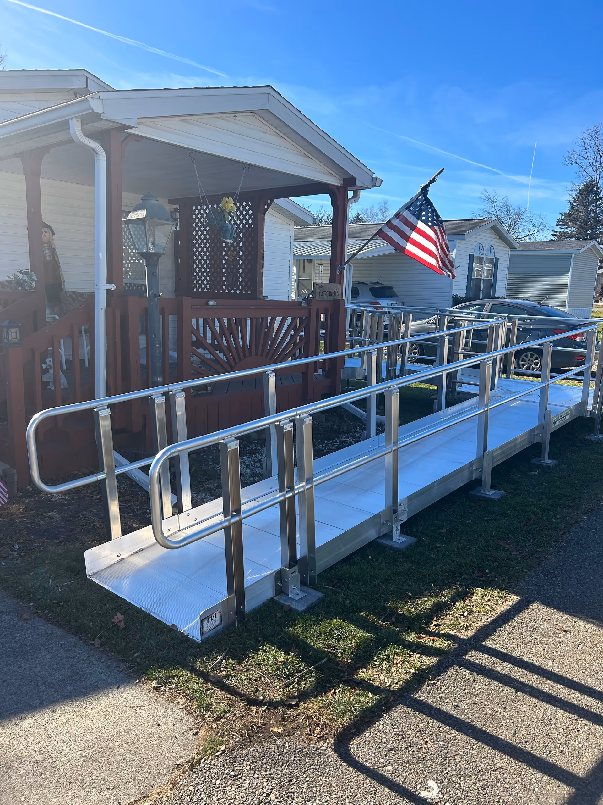 Wheelchair ramp along front porch with railing and an American flag.