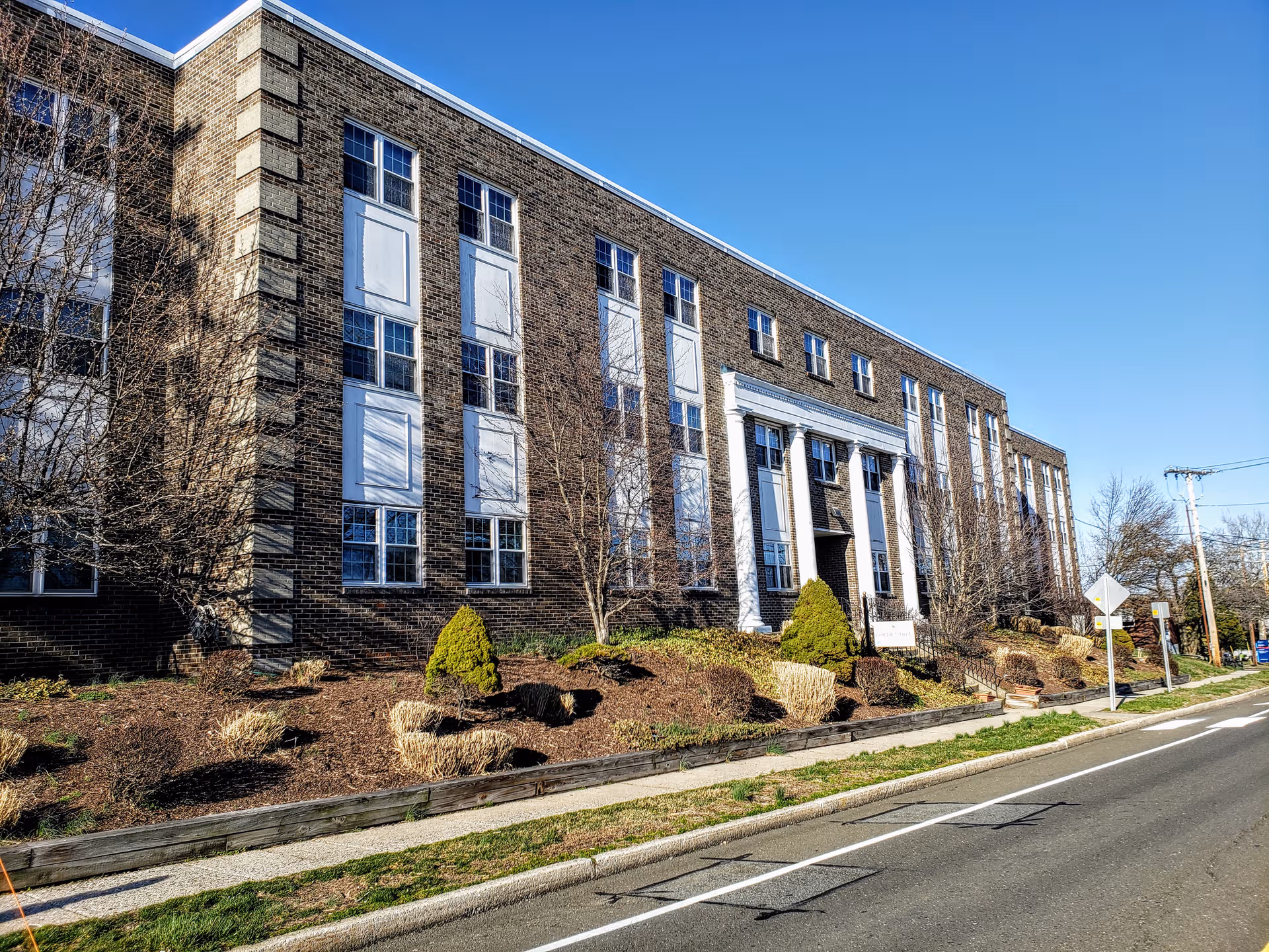 Brick senior living facility exterior with windows, entry, and landscaped front lawn.
