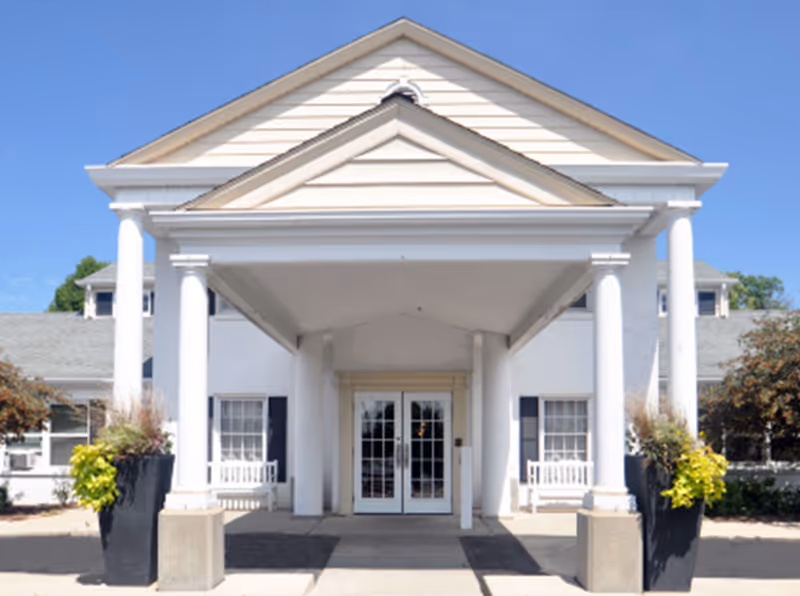 Aria of Brookfield front entrance with white columns, glass doors, and a peaked roof.