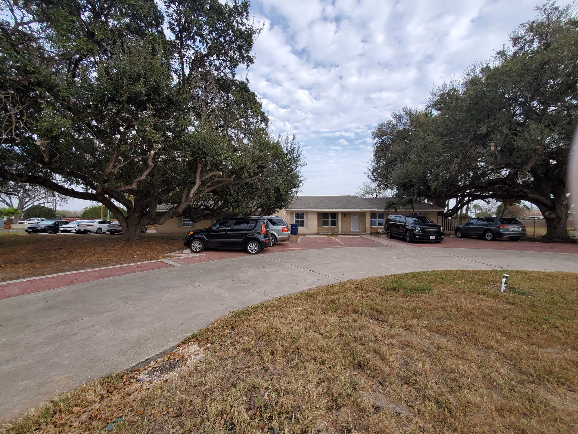 Front view of a single-story building with a curved driveway and parked cars.