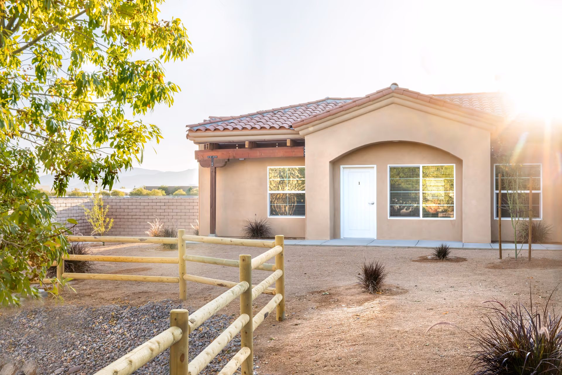 A single-story beige building with a tiled roof and front entrance, desert landscaping.