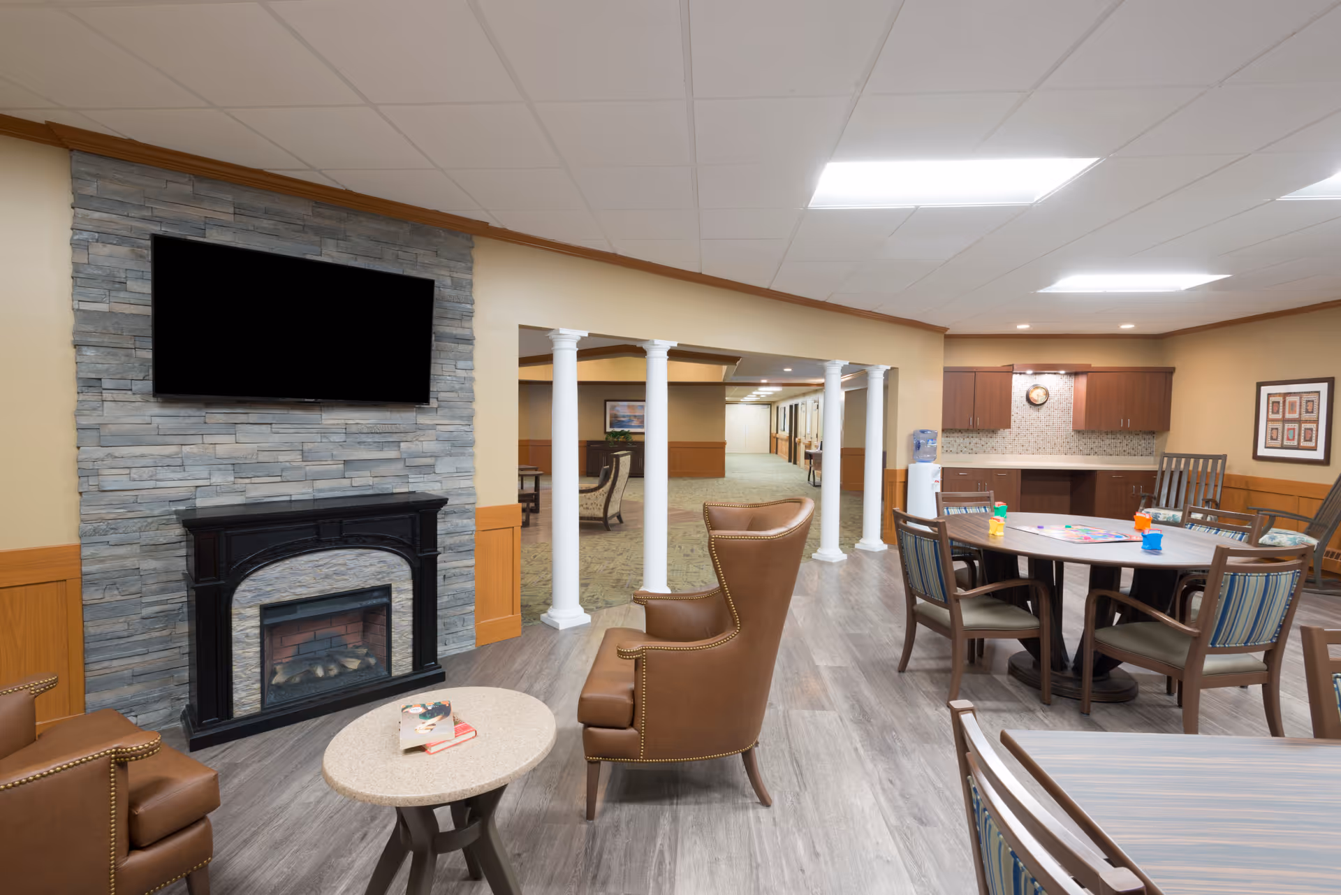 Senior living common area with fireplace, stone wall, TV, and round dining tables.