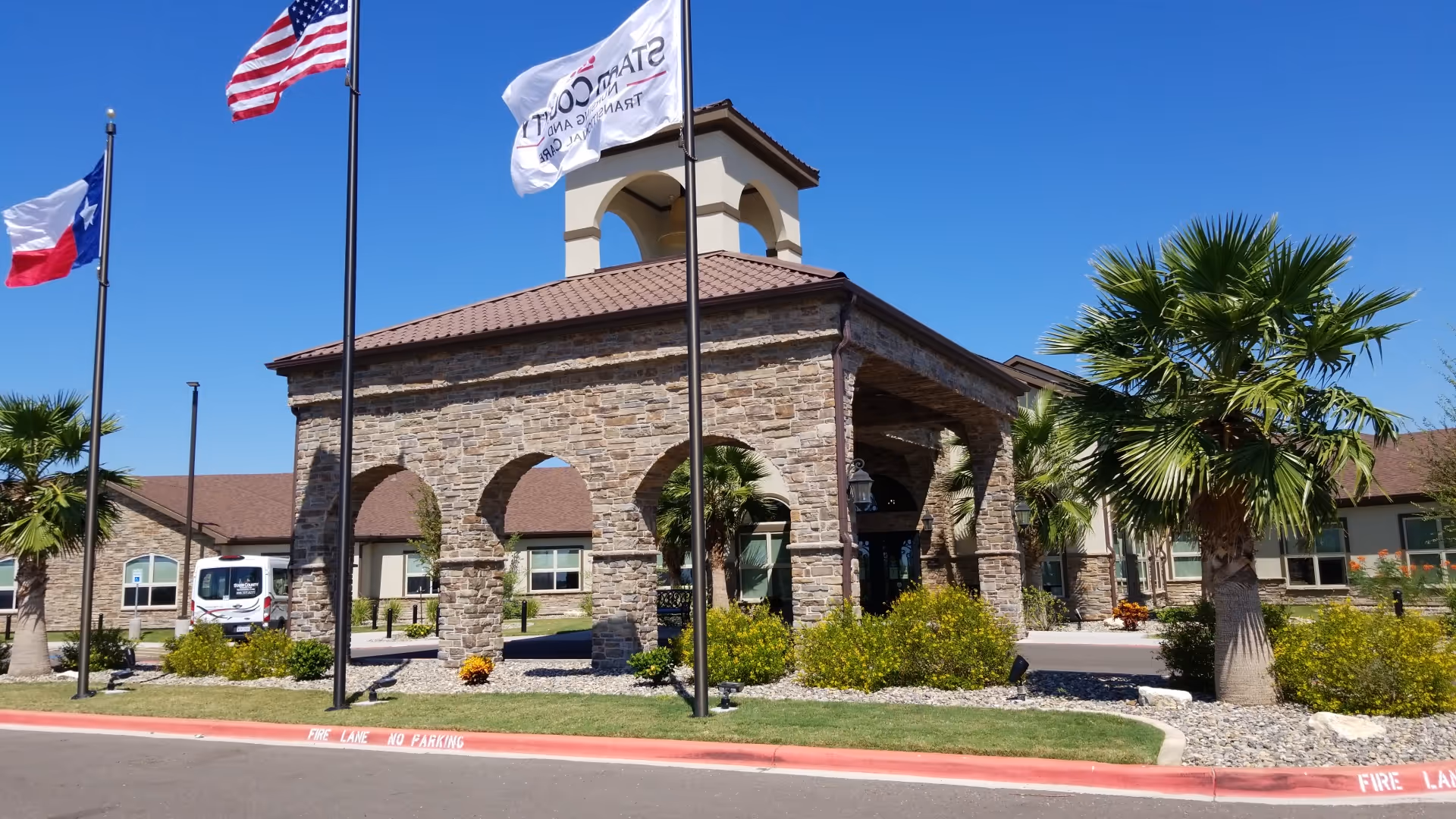 Stone-arched exterior of Starr County Nursing and Transitional Care with flagpoles and palm trees