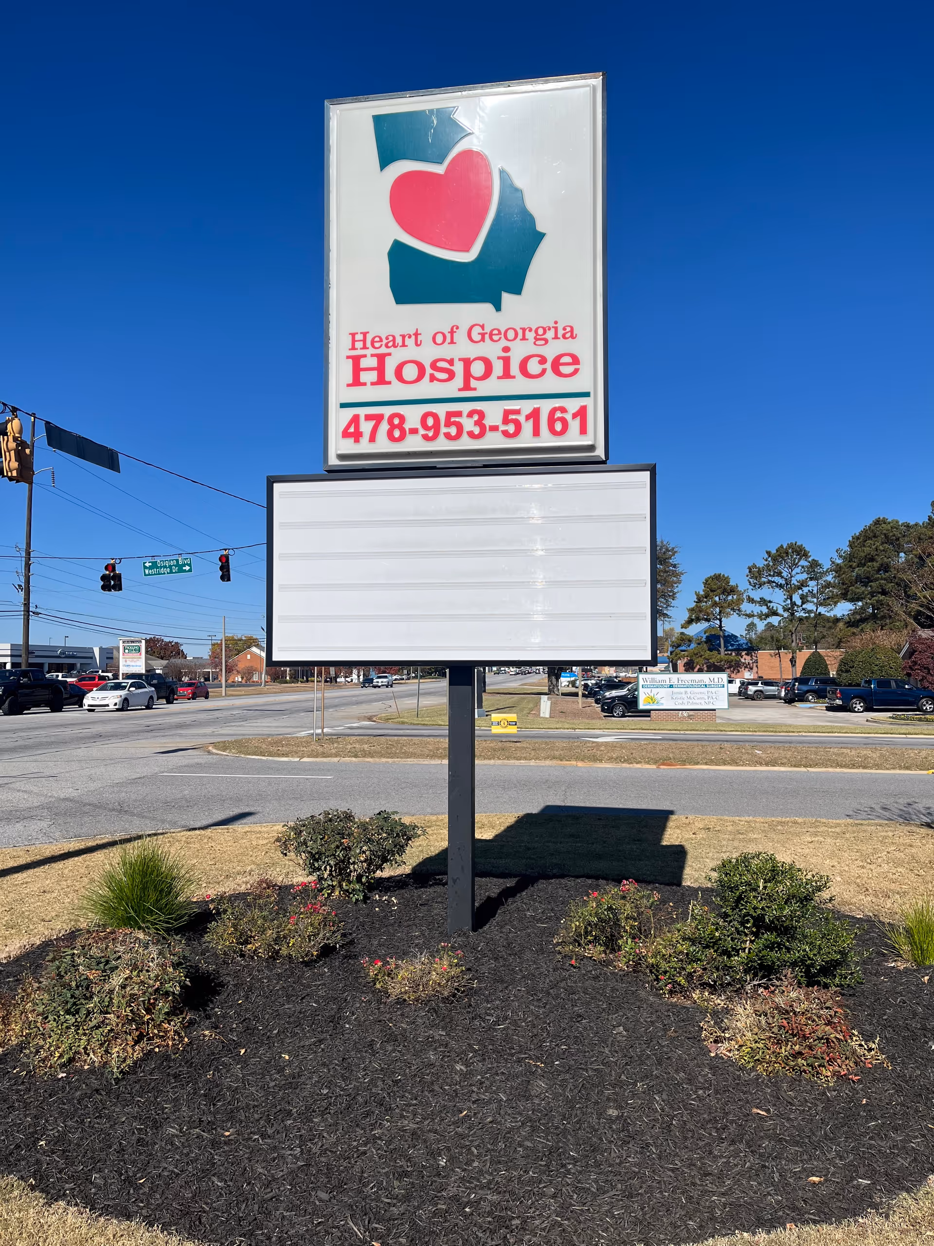 Outdoor Heart of Georgia Hospice sign with heart logo and phone number atop landscaped bed.