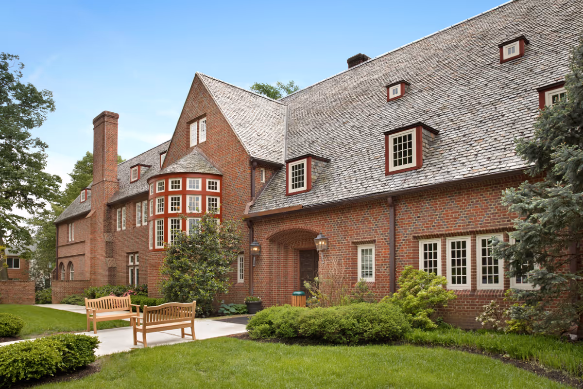 Exterior brick building of The Quadrangle with lawn, benches, and shrubs.