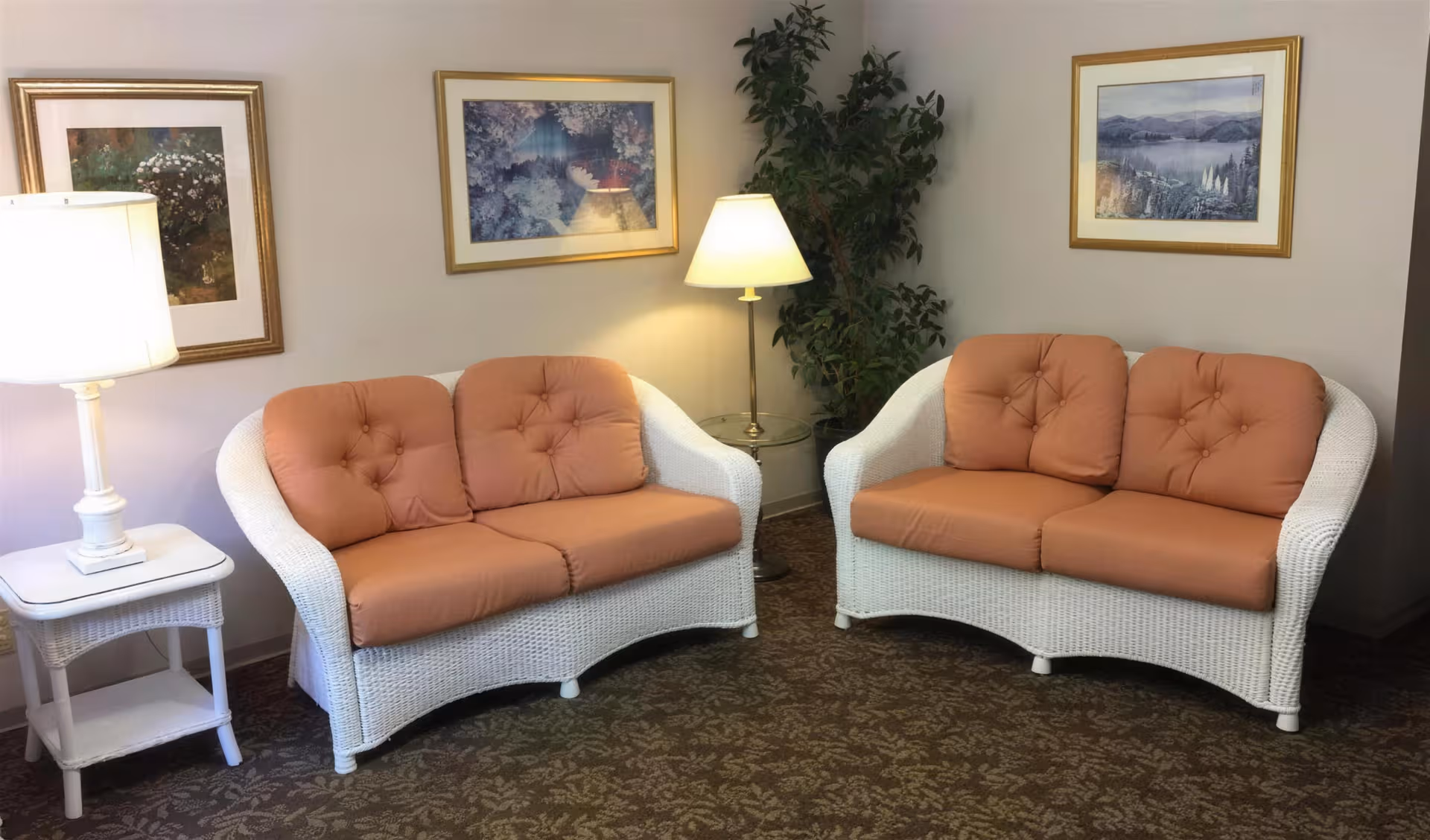 Two peach-cushioned white wicker sofas occupy a cozy lounge with lamps and artwork.