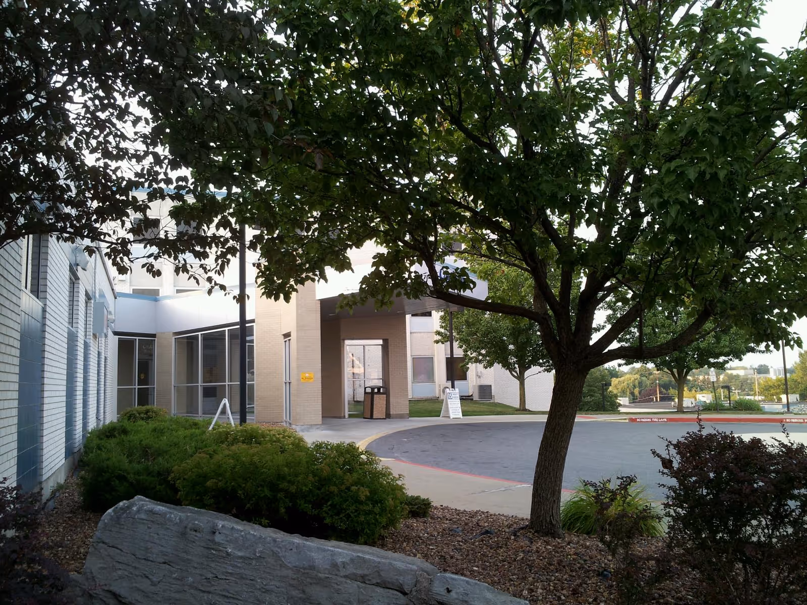 Exterior view of a senior living facility entrance with trees and landscaping.