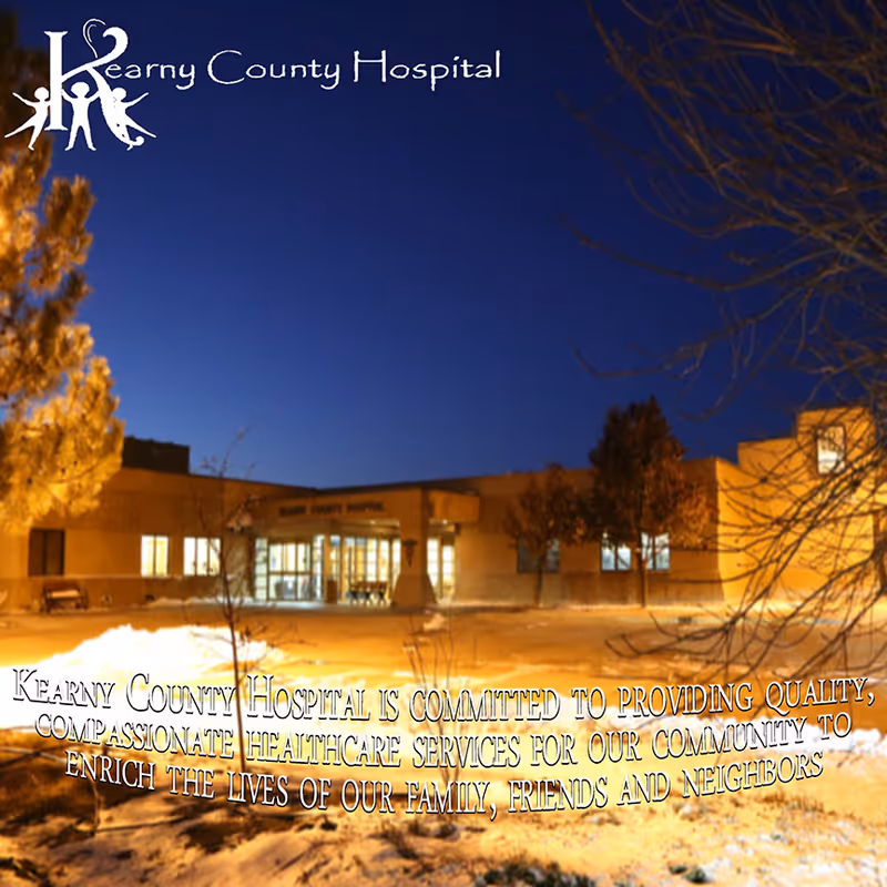 Exterior view of Kearny County Hospital building at dusk with lights on inside. Snow is visible on the ground and trees surround the building. The hospital name is displayed on the building and in the top left corner of the image along with a logo of three figures. Text at the bottom states the hospital's commitment to providing quality, compassionate healthcare services to the community.