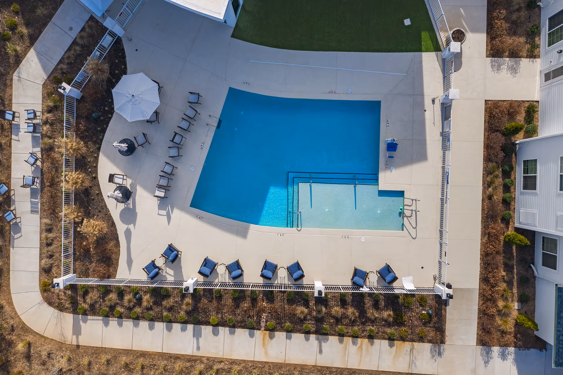 Aerial view of pool, lounge chairs, and umbrellas at a senior living campus.