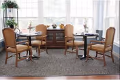 Bright dining room with round tables and upholstered chairs, a sideboard beneath large windows, natural light.
