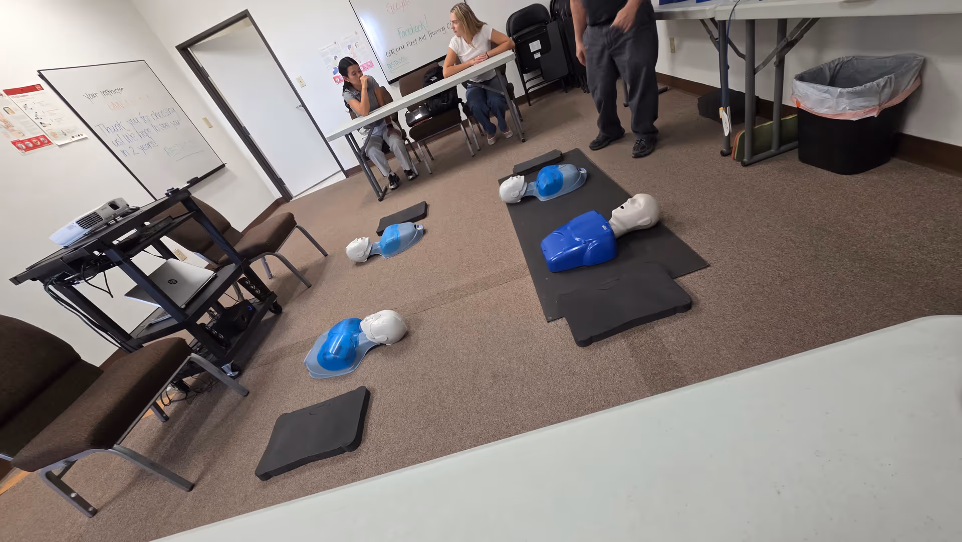 CPR training room with mannequins on mats and participants nearby.