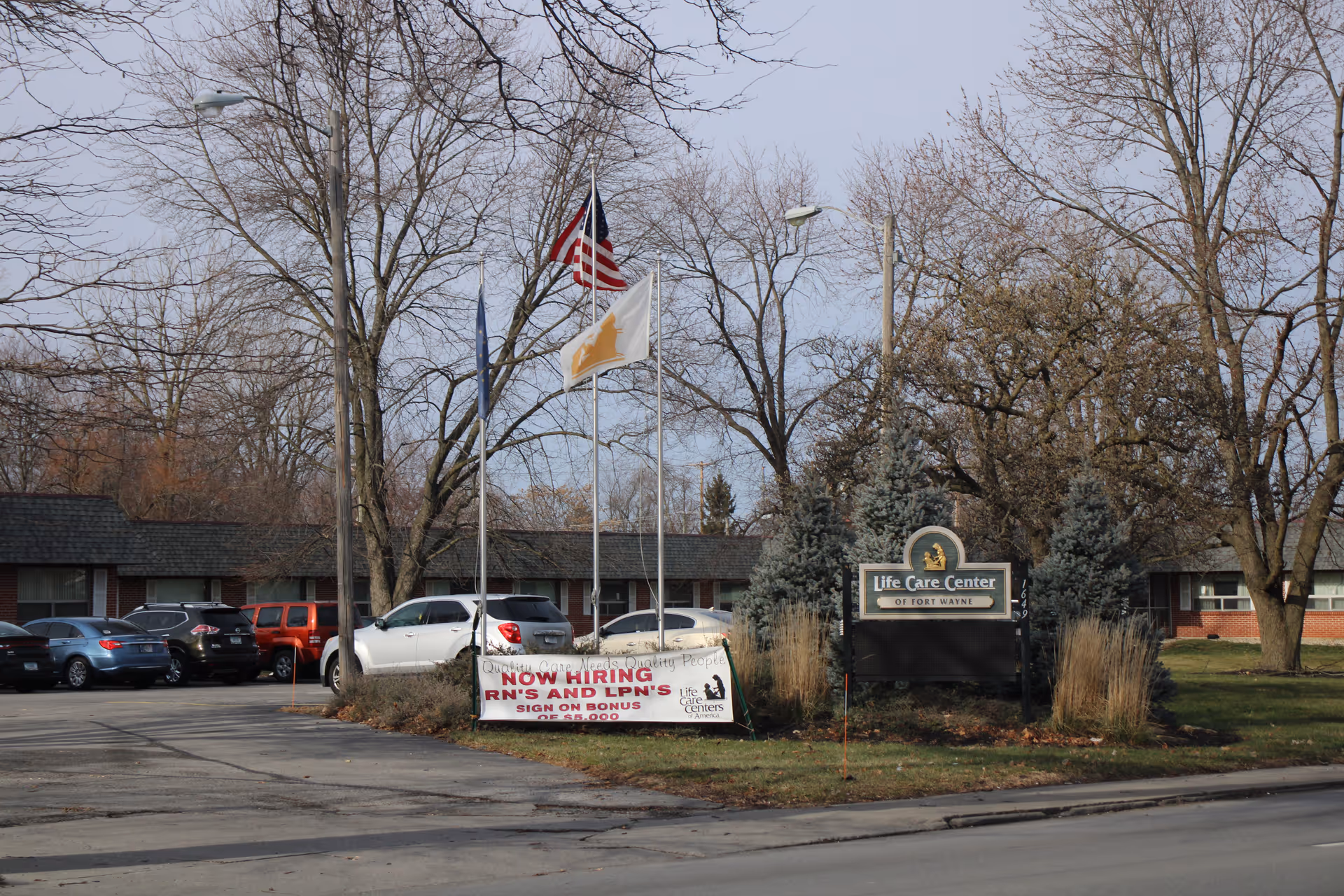 Exterior view of Life Care Center of Fort Wayne with flags, sign, and parked cars.