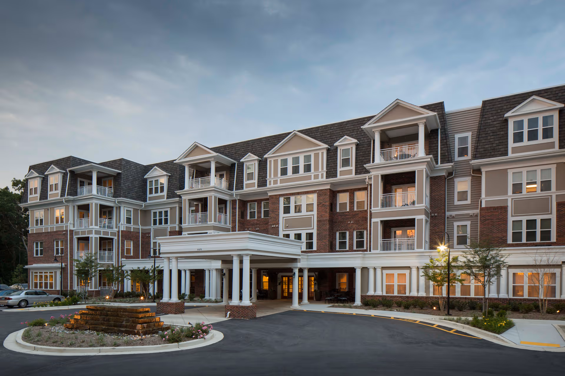 Exterior view of a brick senior living facility with a covered entrance and balconies.