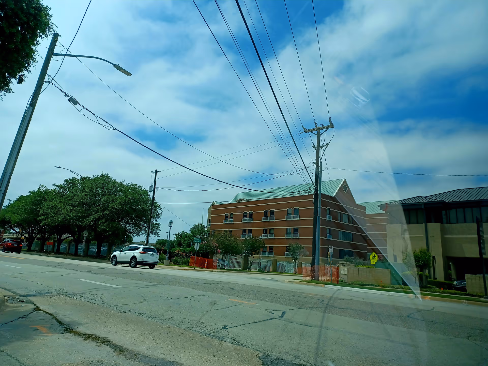 Street view of a brick building across the road with power lines and trees.