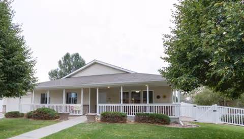 Single-story senior living facility with a covered front porch and white railing, green lawn.