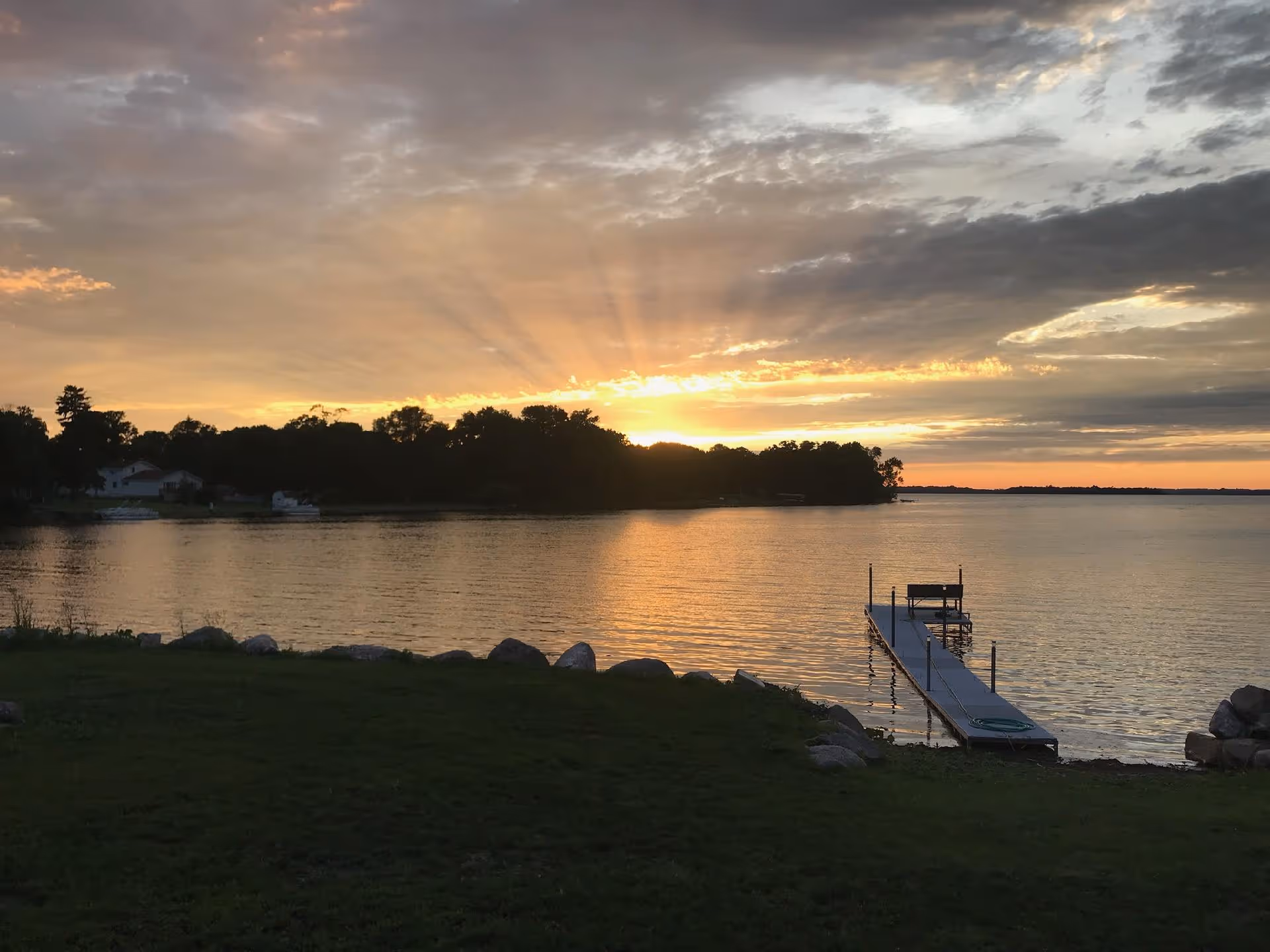 Sunset over a calm lake with a wooden dock extending into the water.