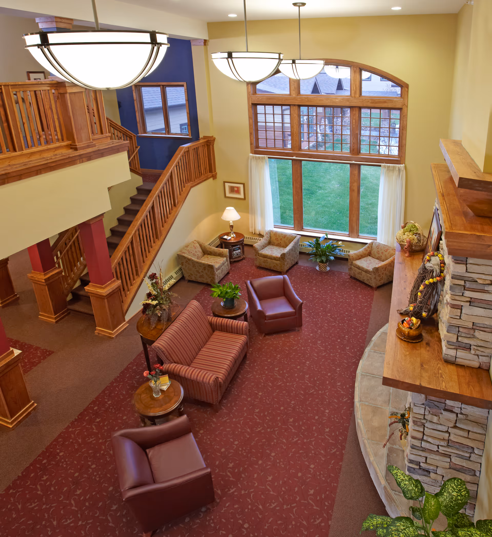 Two-story interior lounge with wooden staircase, red carpet, and large arched windows.