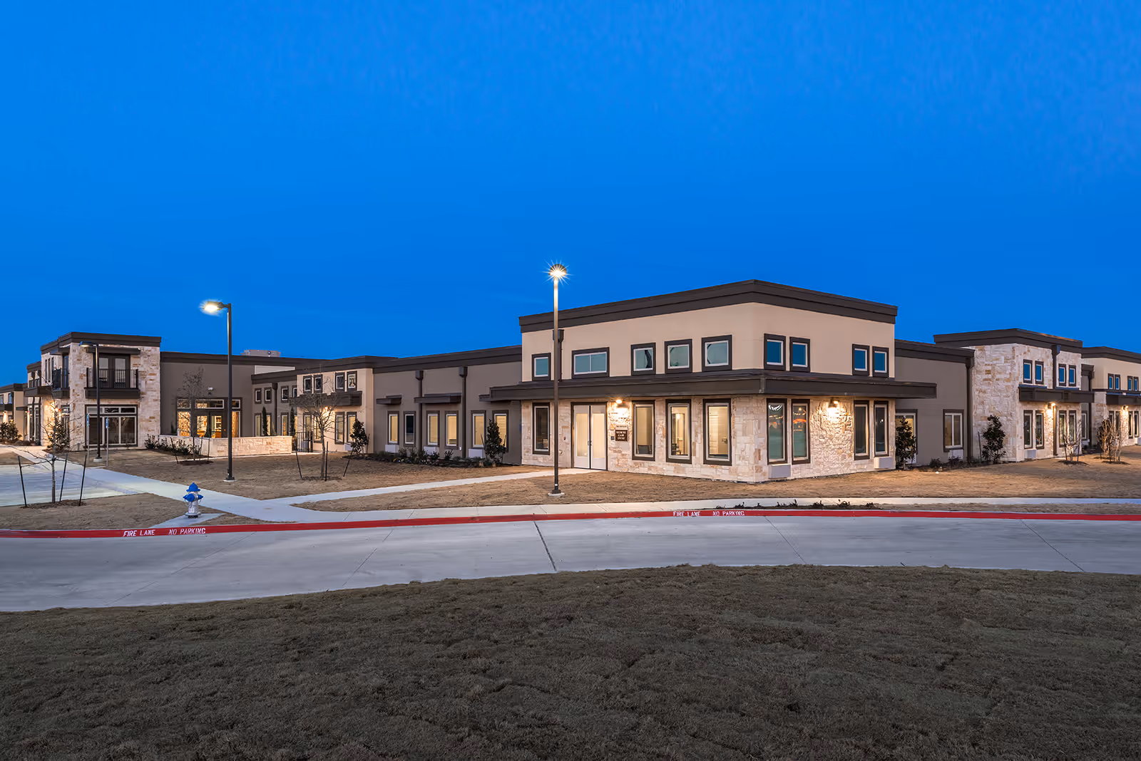 Modern senior living campus exterior at dusk with connected stone and beige buildings.