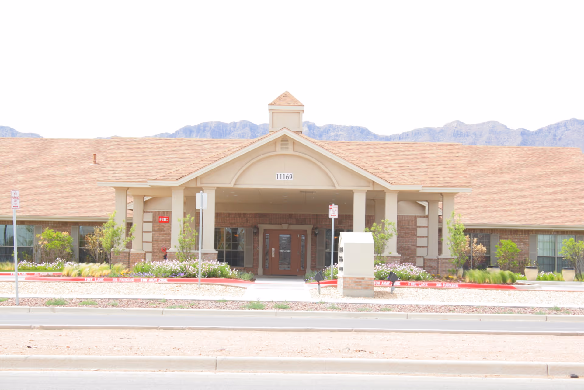 Front view of Los Arcos del Norte Care Center entrance with landscaping and mountains.