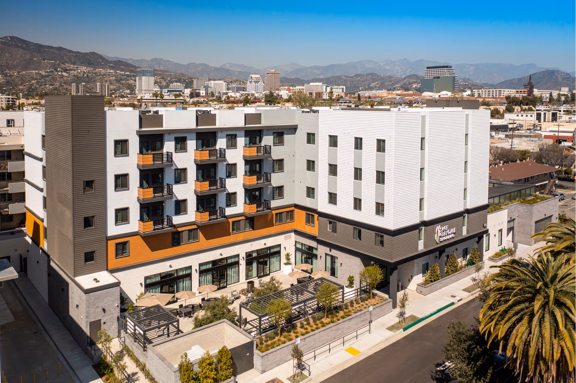 A multi-story Sage Glendale senior living building with balconies and outdoor seating, hillside cityscape background.