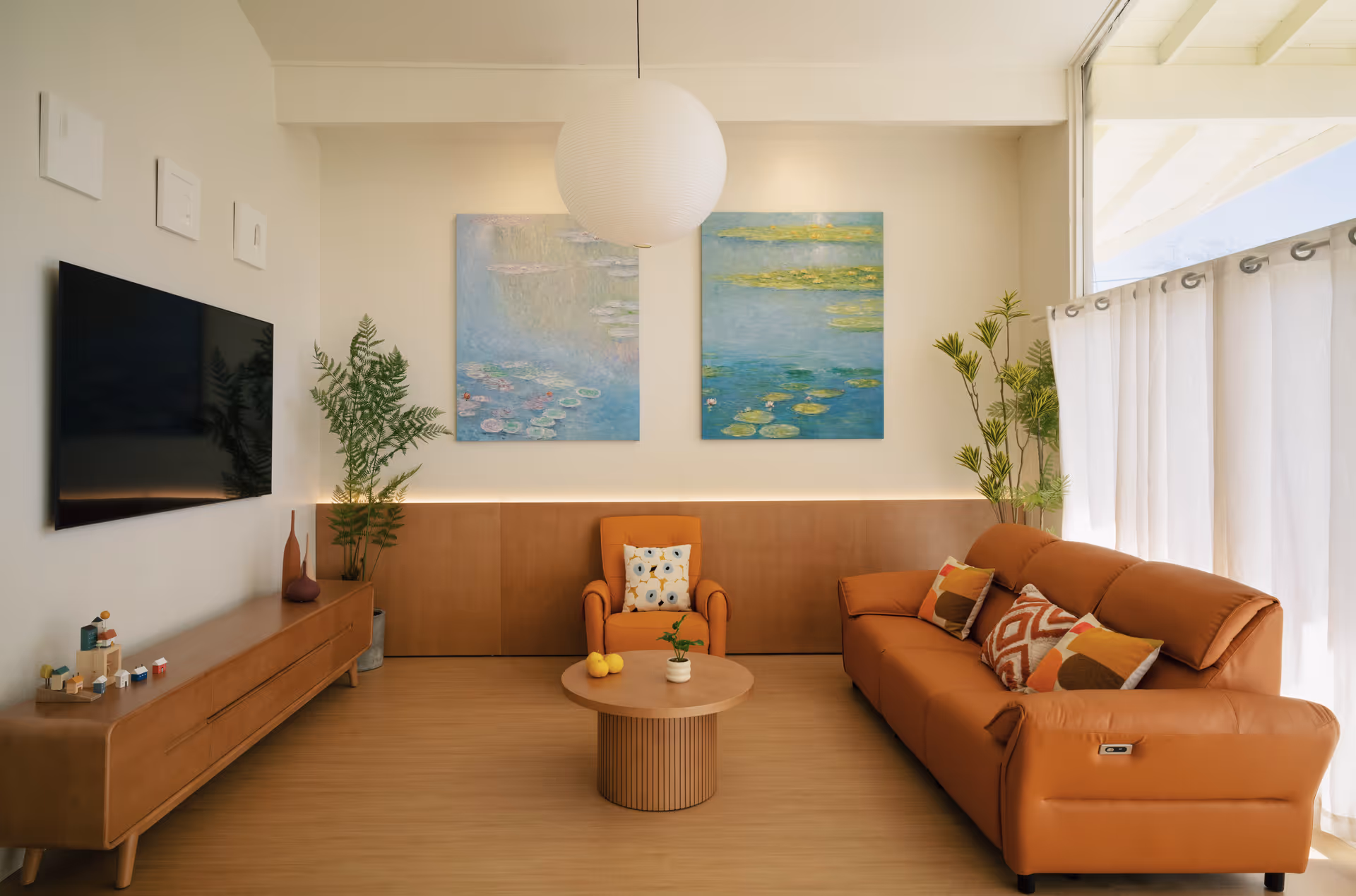 Bright modern living room in a senior care facility with sofa, armchair, plants, and artwork.